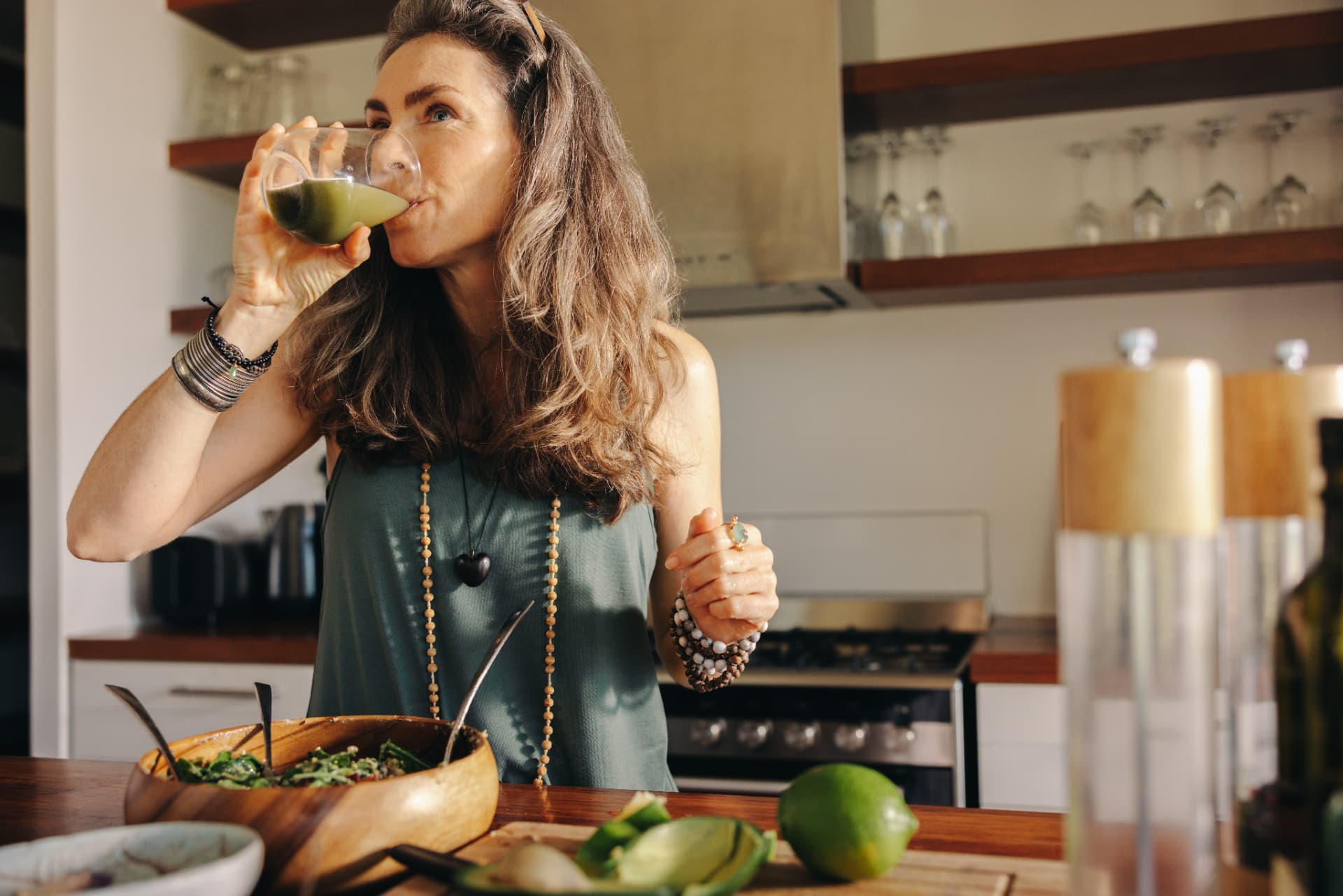 A woman enjoying a fresh green juice in a warm, natural kitchen with wholesome ingredients on the counter