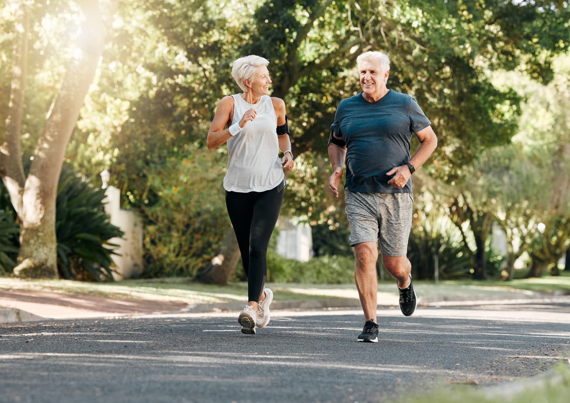 An active older couple jogging together on a sunny tree-lined path